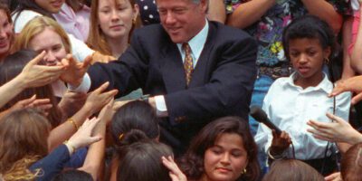 An Image Of President Bill Clinton In The Middle Of A Crowd Of Diverse Individuals, Shaking Outstretched Hands